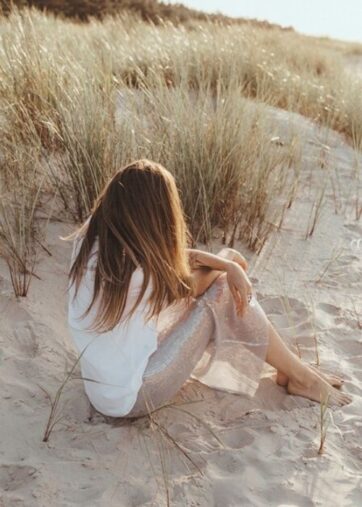 Frau sitzt am Strand mit Blick aufs Meer